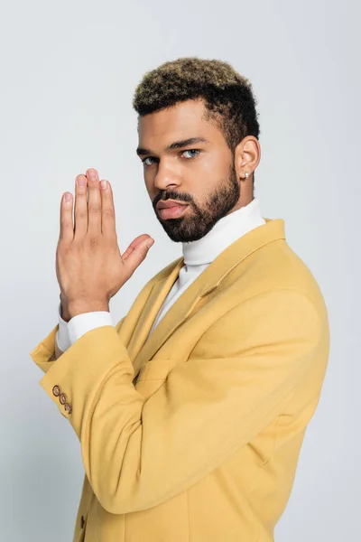 Молодий афроамериканський чоловік у пастельному жовтому блістері з молитовними руками ізольовано на сірому — стокове фото
