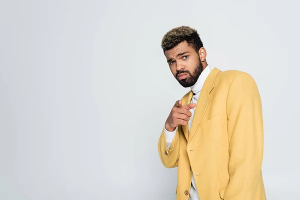 Homme afro-américain barbu avec les yeux bleus dans blazer jaune élégant pointant avec le doigt isolé sur gris — Photo de stock