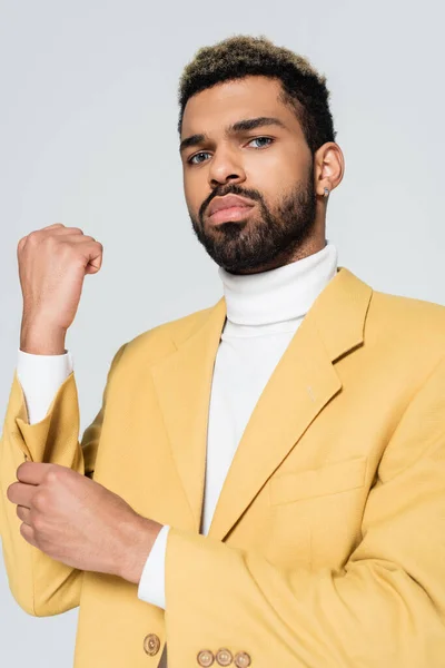 Bearded african american man with blue eyes in stylish yellow blazer adjusting sleeve isolated on grey — Stock Photo