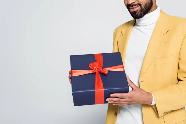 Vista recortada de hombre americano africano alegre en blazer elegante amarillo sosteniendo regalo envuelto aislado en gris - foto de stock