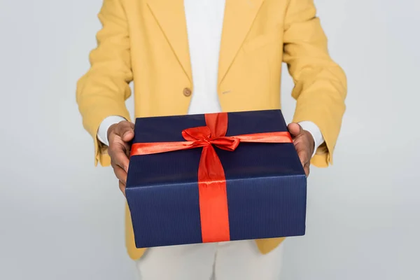 Vista recortada del hombre afroamericano en blazer elegante amarillo sosteniendo regalo envuelto aislado en gris - foto de stock