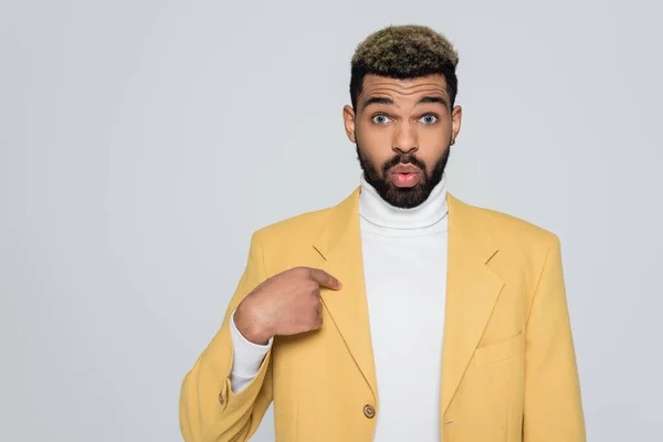 Barbudo hombre afroamericano en cuello alto y blazer con estilo amarillo apuntando a sí mismo aislado en gris - foto de stock