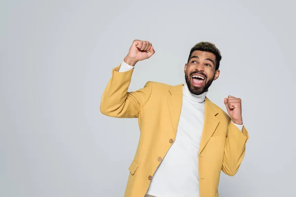 Erstaunt afrikanisch-amerikanischer Mann in Rollkragen und gelbem stylischem Blazer isoliert auf grau — Stockfoto