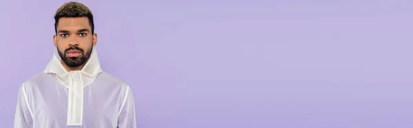 Молодой африканский американец в модной спортивной одежде смотрит в камеру изолированную на фиолетовый, баннер — стоковое фото