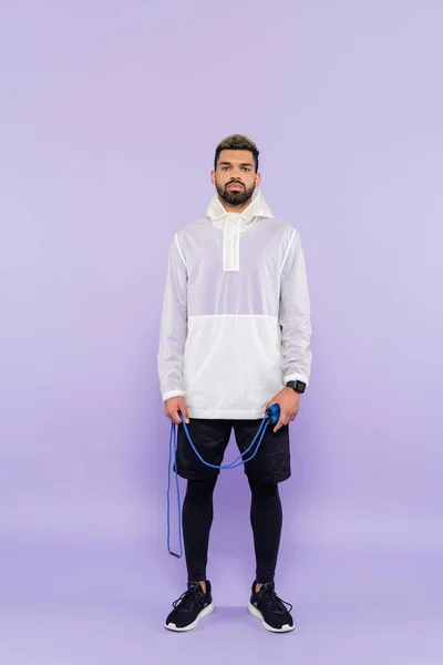 Pleine longueur de jeune homme afro-américain en vêtements de sport à la mode tenant corde à sauter sur violet — Photo de stock