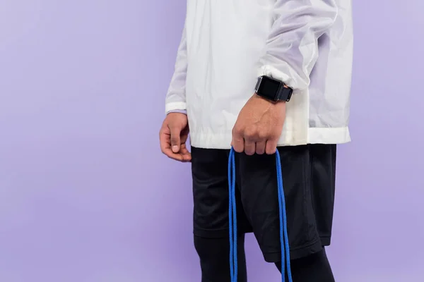 Vista cortada do homem americano africano com relógio inteligente segurando pular corda isolada em roxo — Fotografia de Stock