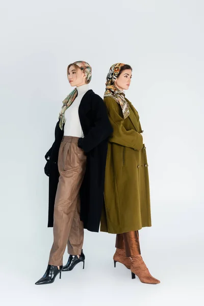 Volle Länge trendiger Frauen in Mänteln und Taschentüchern auf grauem Hintergrund — Stockfoto