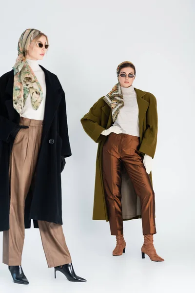 Longitud completa de las mujeres en ropa de moda y gafas de sol sobre fondo gris - foto de stock