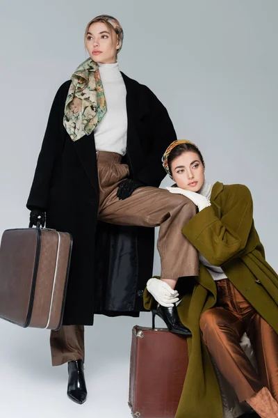 Elegant woman hugging leg of friend standing with vintage suitcase on grey background — Stock Photo