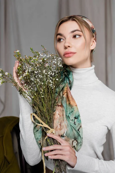 Bonita mulher em kerchief segurando buquê de flores de gypsophila no fundo cinza — Fotografia de Stock