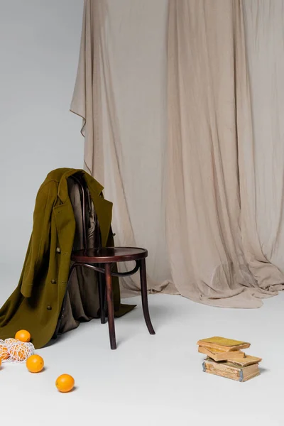 Composição com casaco verde na cadeira perto de livros vintage e laranjas rasgar no chão em fundo cinza com pano — Fotografia de Stock