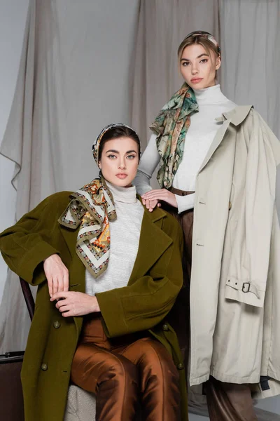 Mujeres con estilo en pañuelos estampados posando cerca de cortina gris sobre fondo - foto de stock