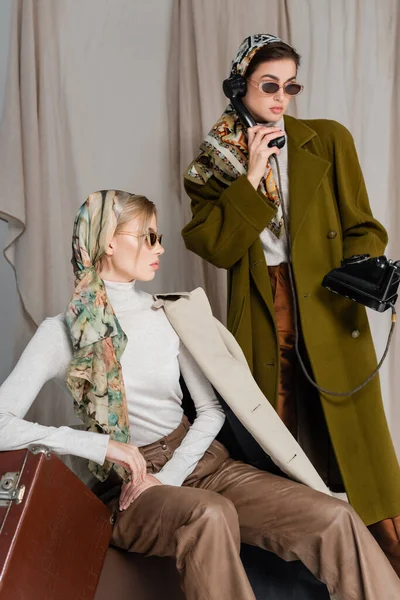 Elegante Frau spricht auf Vintage-Telefon in der Nähe Freund auf grauem Hintergrund mit Vorhang — Stockfoto