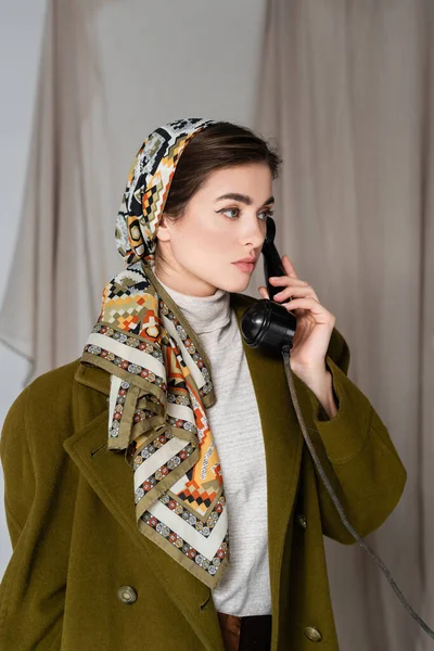 Femme élégante en foulard à motifs faisant appel au téléphone vintage sur fond gris avec draperie — Photo de stock