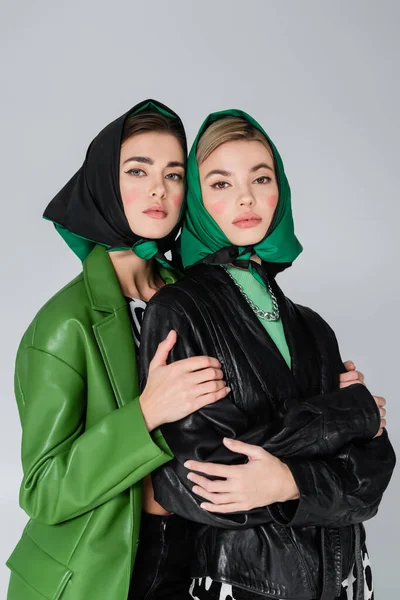 Woman in black kerchief embracing stylish friend while looking at camera isolated on grey — Stock Photo