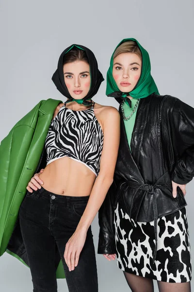 Trendy women in animal print clothing posing with hands on hips isolated on grey — Stock Photo