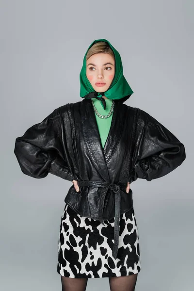 Trendy woman in leather jacket and green kerchief posing with hands on waist isolated on grey — Stock Photo