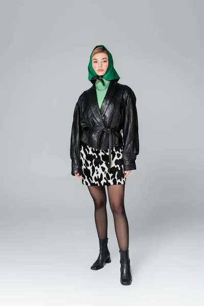 Longitud completa de la mujer en chaqueta de cuero negro y falda de impresión animal sobre fondo gris - foto de stock