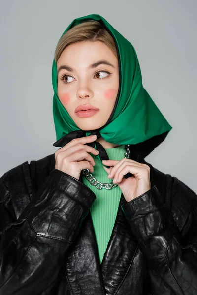 Mujer con maquillaje atando pañuelo verde y mirando hacia otro lado aislado en gris - foto de stock