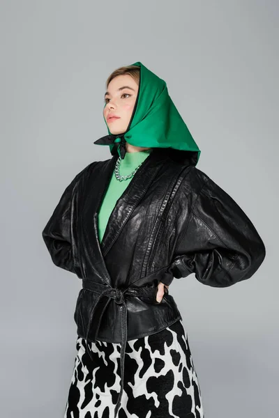 Jovem mulher em lenço verde e jaqueta de couro preto de pé com as mãos na cintura isolada em cinza — Fotografia de Stock