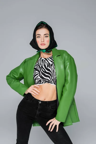 Mujer de moda en chaqueta verde y estampado de cebra top de pie con la mano en la cintura aislado en gris - foto de stock