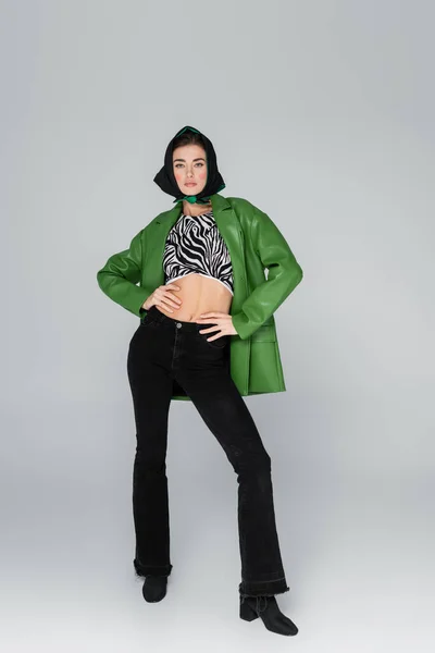 Vista completa de la mujer de moda en pañuelo negro y chaqueta verde sobre fondo gris - foto de stock