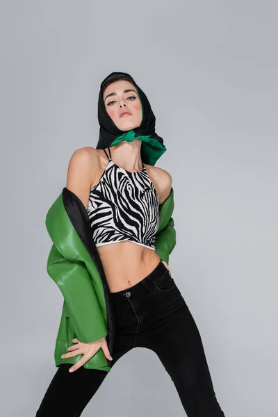Trendfrau in Zebra-Print, bauchfreiem Oberteil und Halstuch blickt vereinzelt in die Kamera auf grau — Stockfoto