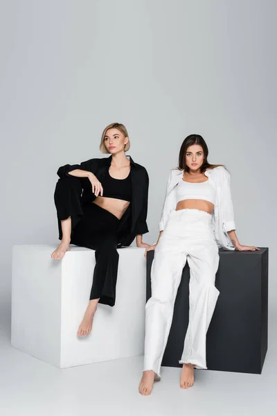 Longitud completa de las mujeres descalzas en ropa blanca y negra posando sobre cubos sobre fondo gris — Stock Photo