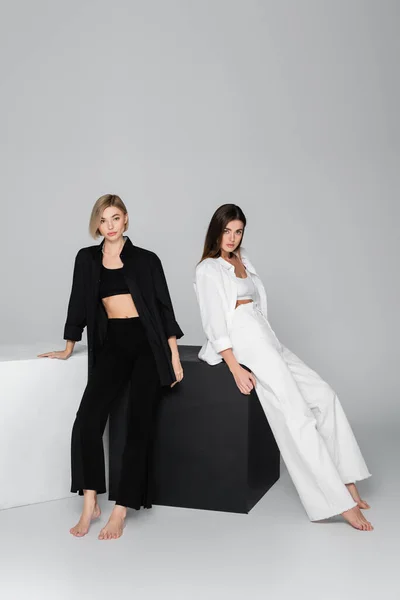 Повна довжина босоногих жінок у стильному одязі, що позує біля чорно-білих кубиків на сірому фоні — Stock Photo