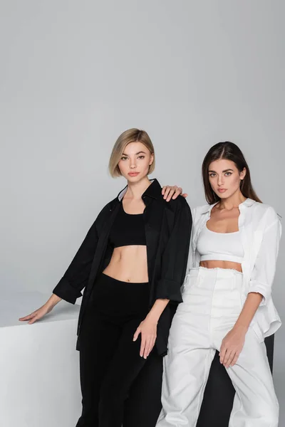 Brunette and blonde women in black and white clothes posing near cubes isolated on grey — Stock Photo