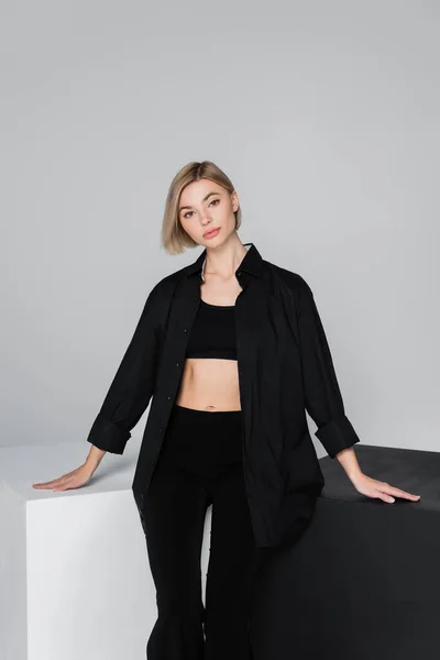 Young woman in bra and shirt looking at camera near black and white cubes isolated on grey — Stock Photo