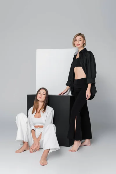 Barefoot models in shirts and trousers posing near black and white cubes on grey background — Stock Photo