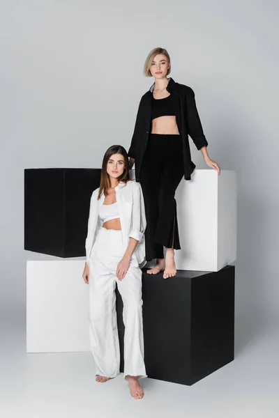 Full length of woman standing on cube near friend in white clothes on grey background — Stock Photo