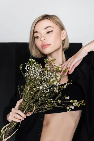 Joven rubia posando con ramo de flores de gypsophila sobre fondo negro y gris - foto de stock