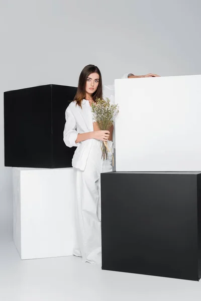 Брюнетка женщина с цветами, стоящими рядом с черно-белыми кубиками на сером фоне — стоковое фото