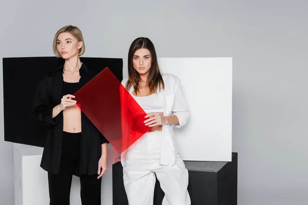 Donne alla moda in possesso di vetro rosso vicino a cubi bianchi e neri isolati su grigio — Foto stock
