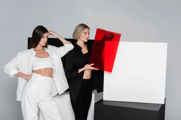 Femme tenant du verre rouge debout avec un ami près de cubes noirs et blancs isolés sur gris — Photo de stock