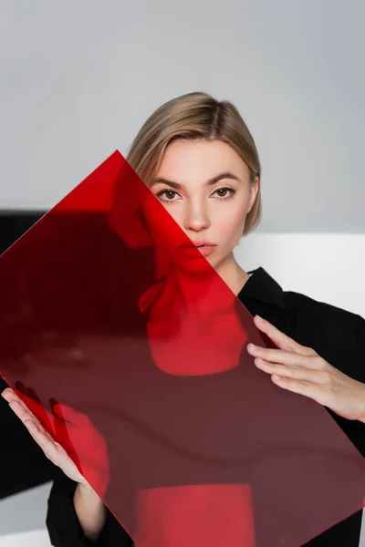 Mulher loira com vidro vermelho olhando para a câmera no cinza com preto e branco — Fotografia de Stock