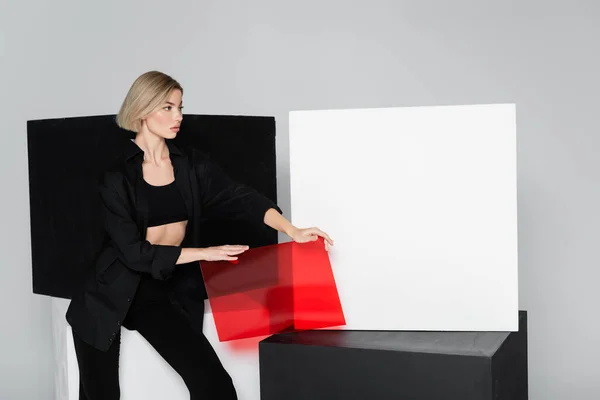 Женщина в черной одежде, держа красное стекло возле кубов, изолированных на сером — стоковое фото