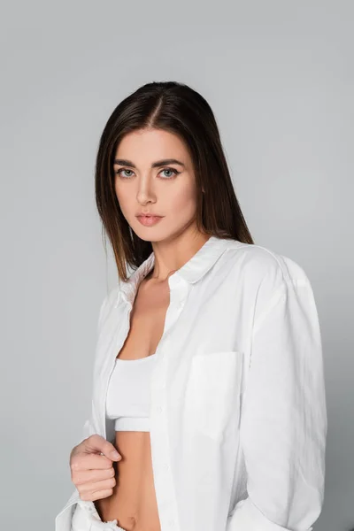 Brunette femme en soutien-gorge blanc et chemise regardant caméra isolée sur gris — Photo de stock