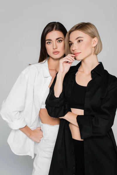 Brunette and blonde woman posing in black and white clothes isolated on grey — Stock Photo