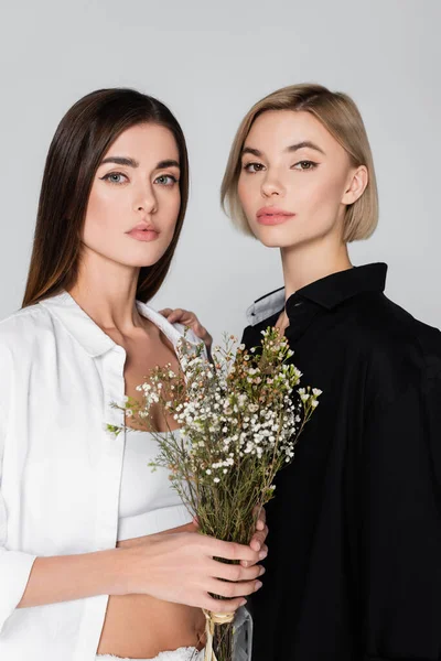 Mujer con estilo en camisas blancas y negras mirando a la cámara cerca de flores de gypsophila aisladas en gris - foto de stock