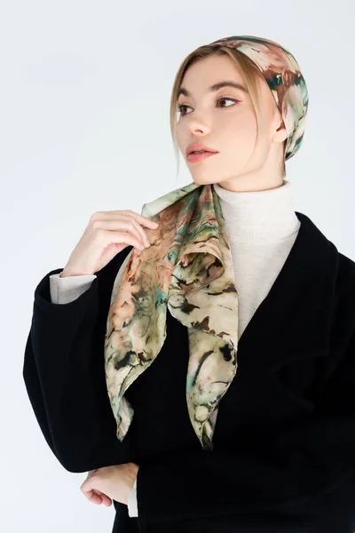 Mujer con estilo en pañuelo para la cabeza y abrigo negro mirando hacia otro lado aislado en gris - foto de stock