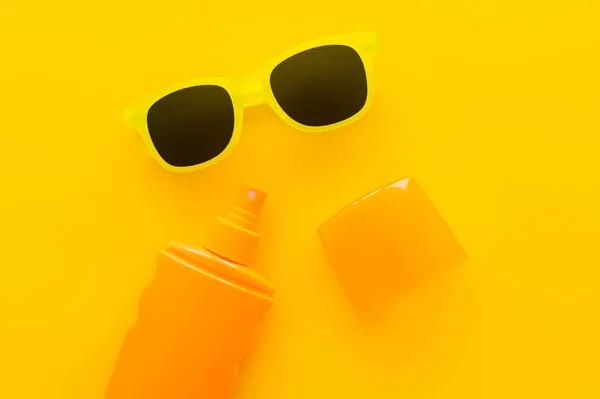 Vue du dessus des lunettes de soleil et de la crème solaire sur fond jaune — Photo de stock