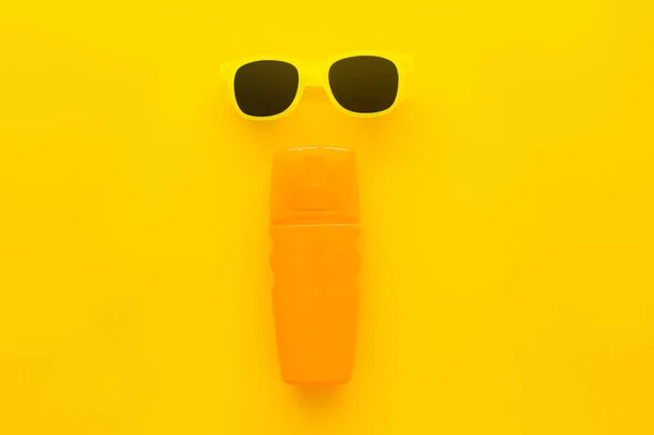 Top view of sunglasses and bottle of sunscreen on yellow background — Stock Photo