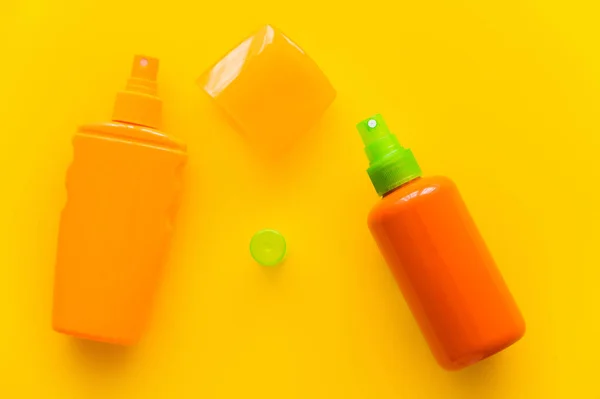 Vue du dessus des bouteilles et des casquettes de crème solaire sur fond jaune — Photo de stock