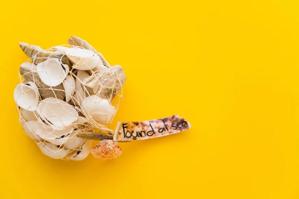 Top view of seashells in net with found at sea lettering on yellow background — Stock Photo