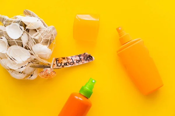 Top view of seashells with found at sea lettering near sunscreens on yellow background — Stock Photo