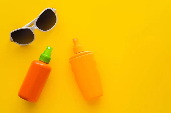 Vue du dessus des écrans solaires près des lunettes de soleil sur fond jaune — Photo de stock