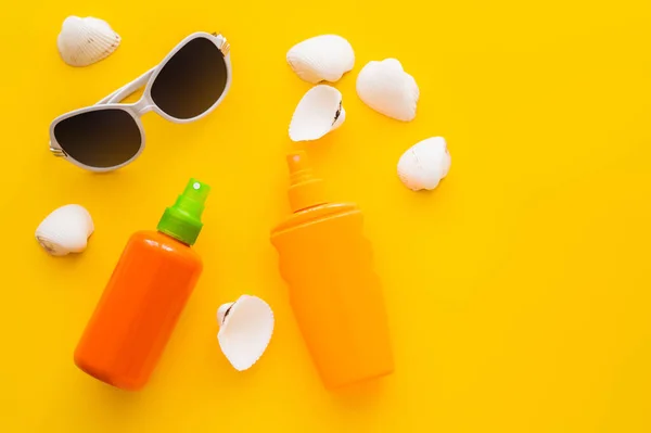 Vista dall'alto di occhiali da sole vicino a creme solari e conchiglie su sfondo giallo — Foto stock